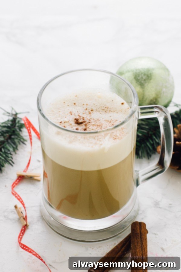 This Boozy Christmas Spiced Eggnog will become your new favourite eggnog! It's warm, frothy, and flavored with spiced rum! Close-up of Spiced Eggnog in a transparent glass mug, showing its frothy top and rich texture.