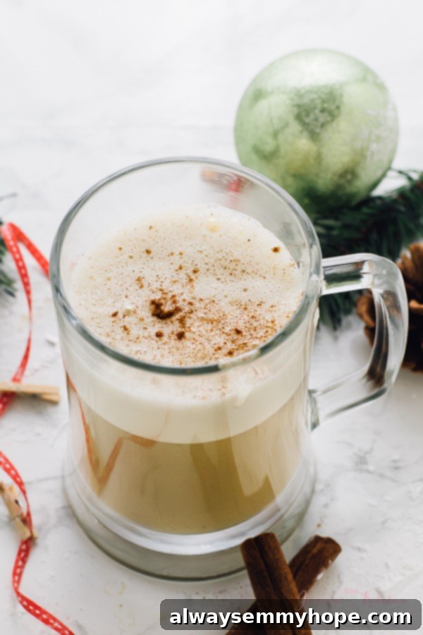 This Boozy Christmas Spiced Eggnog will become your new favourite eggnog! It's warm, frothy, and flavored with spiced rum! A festive glass mug filled with Boozy Christmas Spiced Eggnog, adorned with a cinnamon stick, ready for the holidays.
