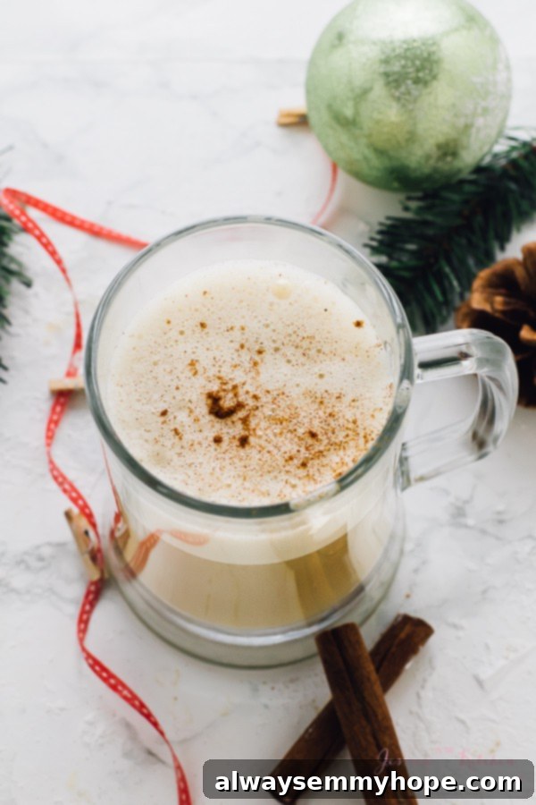 This Boozy Christmas Spiced Eggnog will become your new favourite eggnog! It's warm, frothy, and flavored with spiced rum! Top-down view of a glass mug filled with frothy Boozy Christmas Spiced Eggnog, garnished with a sprinkle of nutmeg on a festive background.