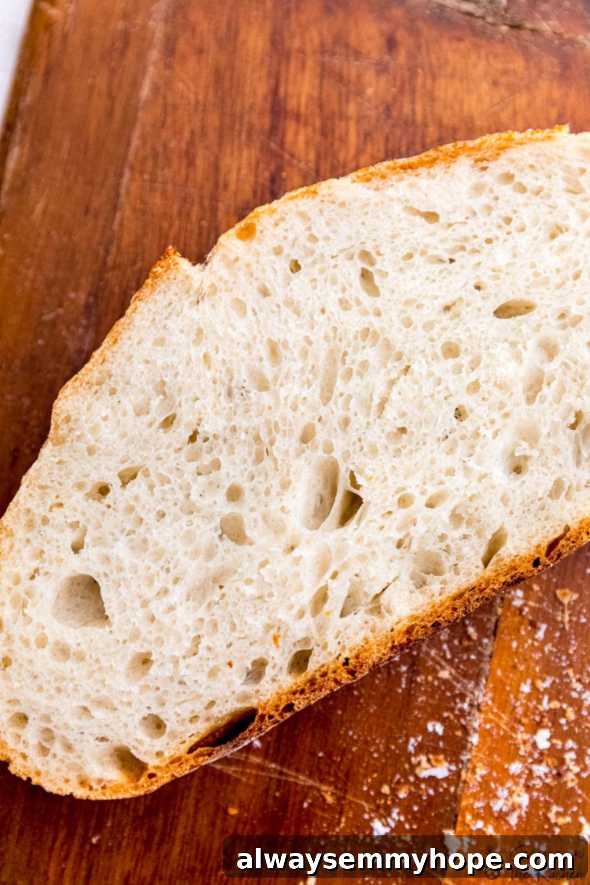 Effortless Dutch Oven Artisan Bread 7 Single slice of no knead bread on a wooden cutting board, showcasing its light and airy texture.