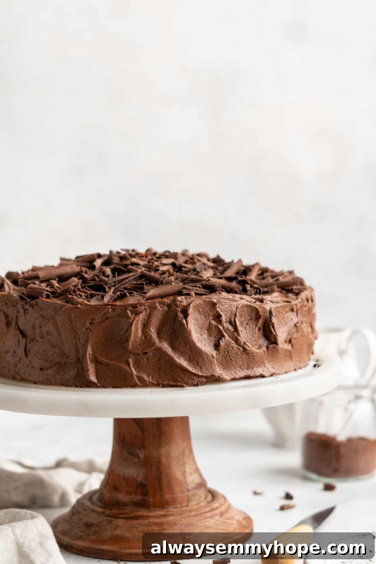 A freshly frosted two-layer vegan chocolate cake proudly displayed on a cake stand, with its rich, dark frosting creating a stunning contrast.