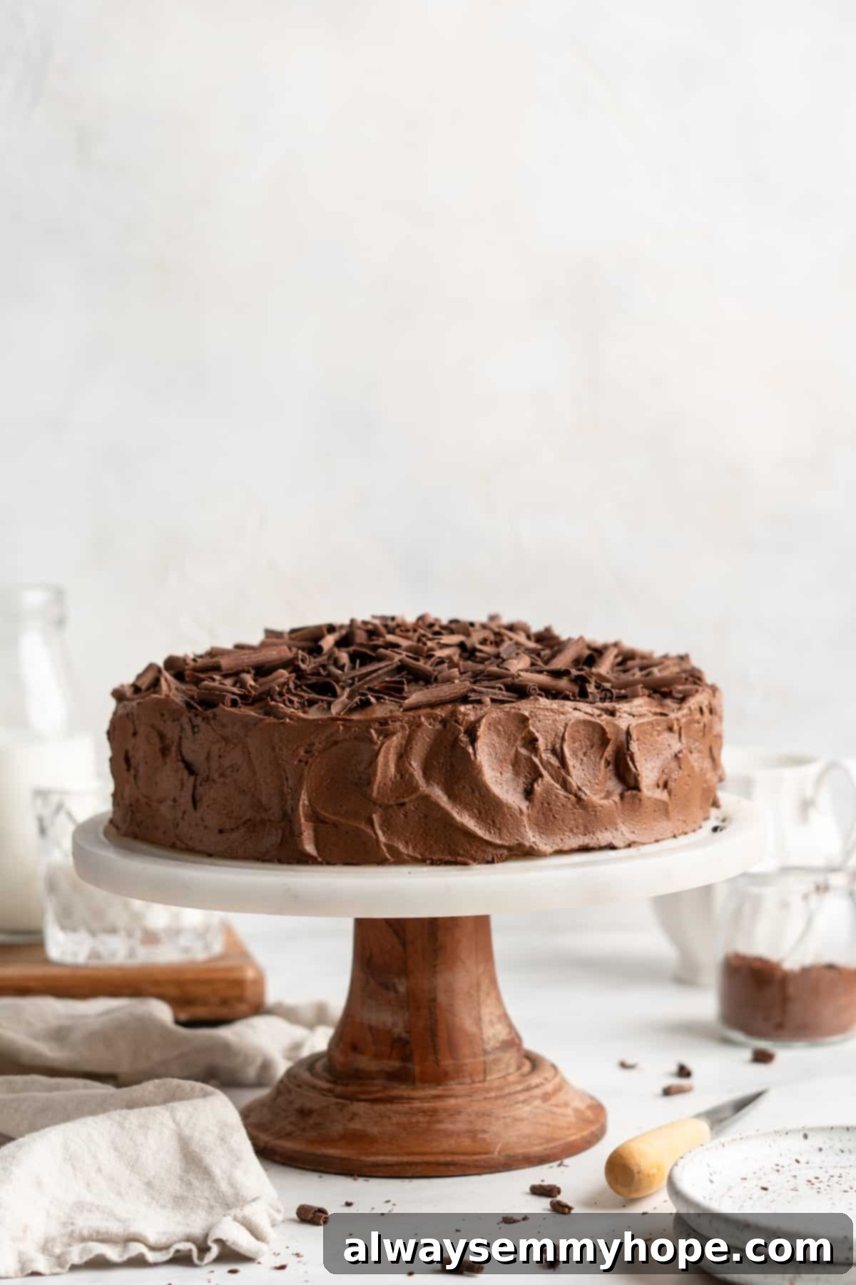 A beautifully frosted whole vegan chocolate cake sits on a elegant cake stand, ready to be sliced and served.