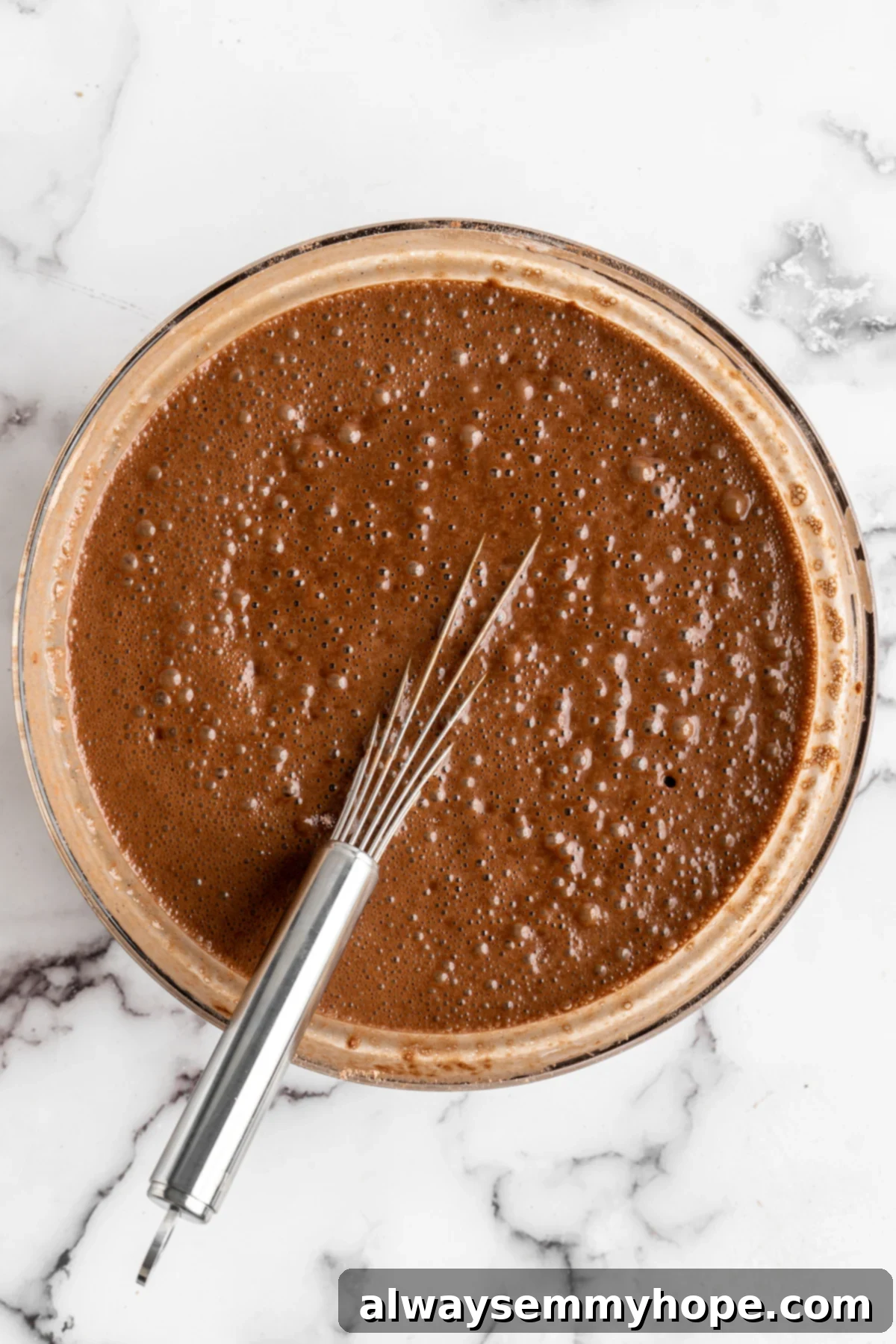 This vegan chocolate cake recipe is the best you'll ever try and the easiest too! Make it yourself and find out why it's a reader favorite. Chocolate cake batter in glass mixing bowl with whisk.