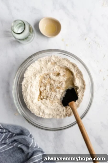 Dry pizza dough ingredients (flour, yeast, salt, sugar, garlic powder) in a large mixing bowl with a well created in the center, and wet ingredients (warm water, olive oil) being poured in.