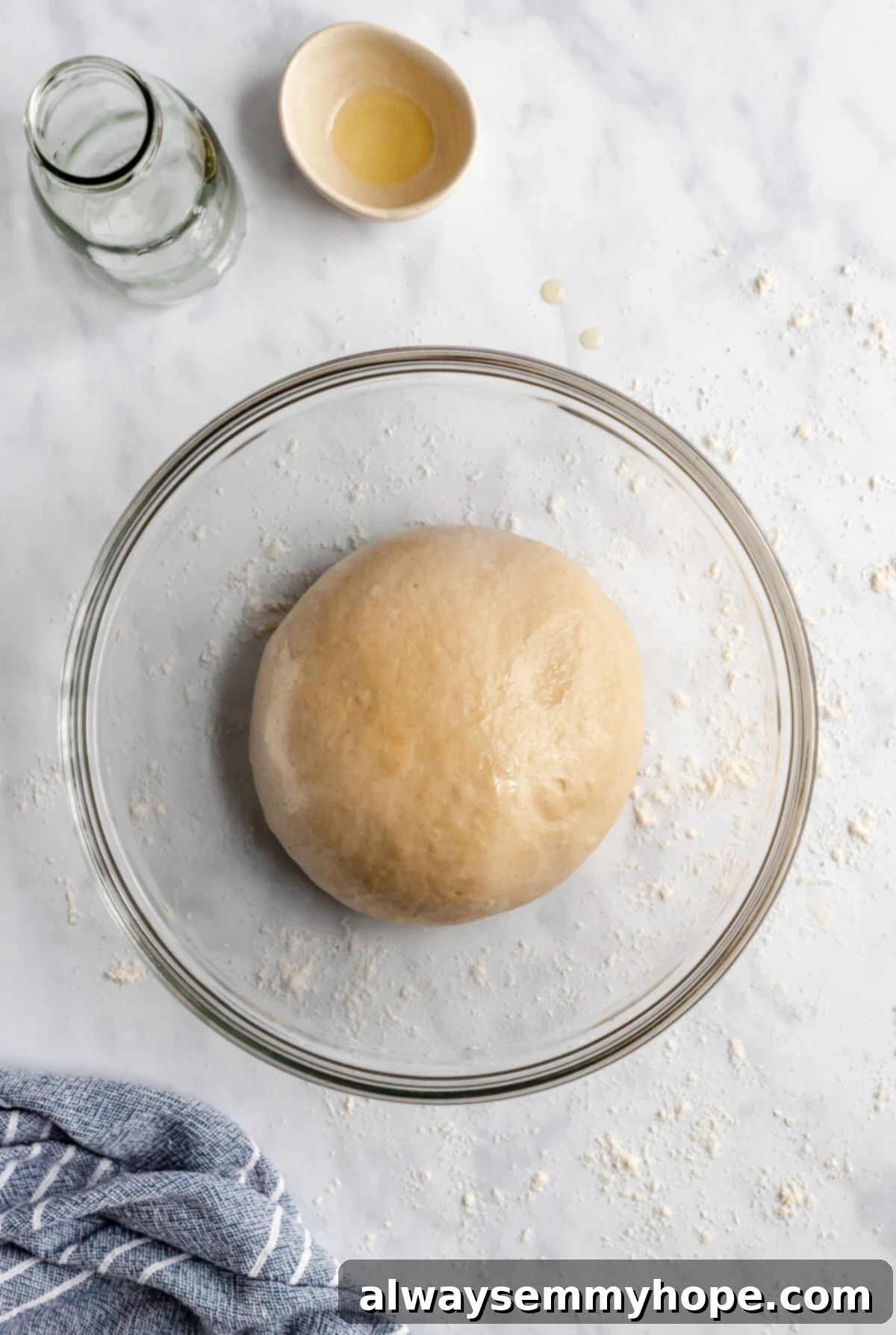 A close-up, top-down view of pizza dough rising in a large glass bowl, covered with plastic wrap, showing its expanded and airy texture.