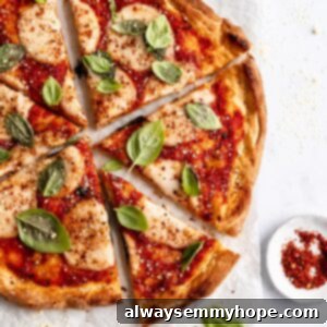 Overhead closeup shot of vegan pizza sliced with one slice slightly pulled out. Scattered basil around, and on parchment paper on a baking sheet.