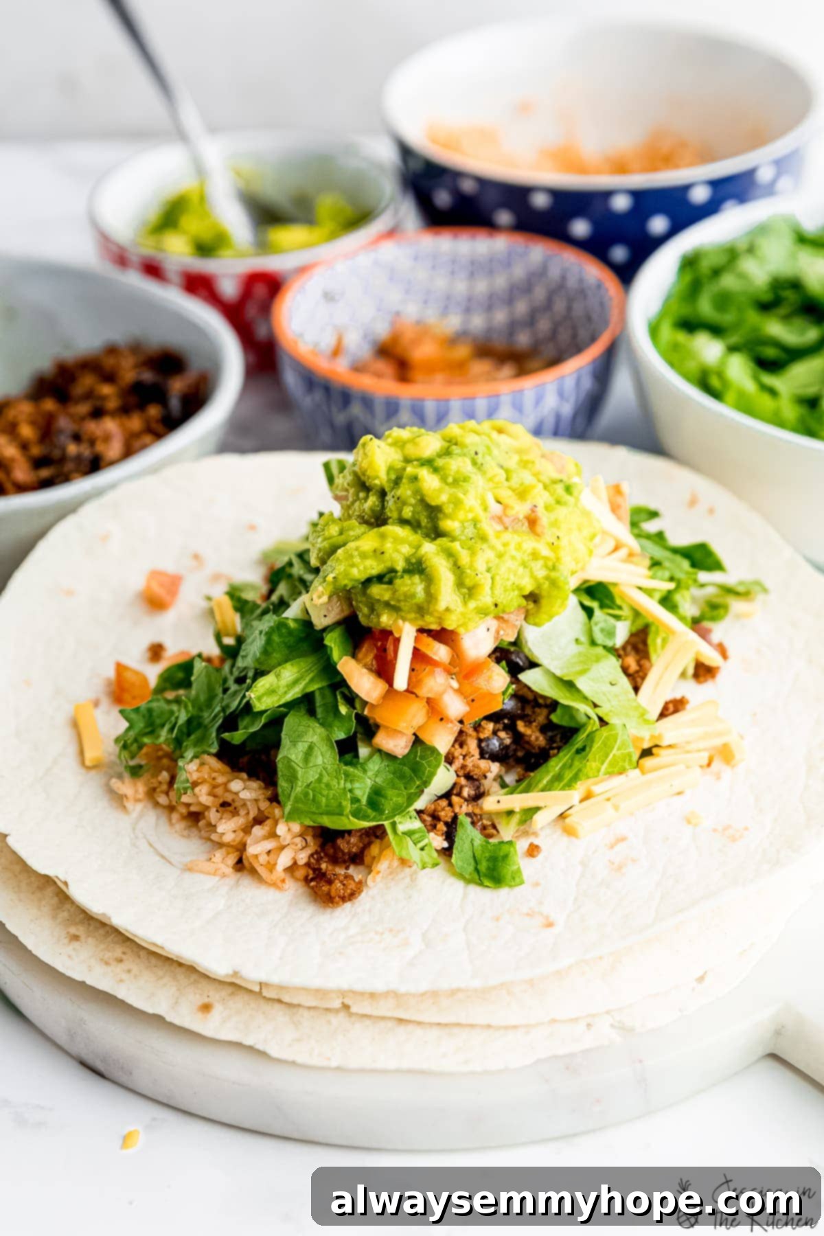 These vegan burritos are packed with walnut “meat”, cheese, beans, seasoned rice, and all your favourite fixings. Perfect for meal prep! A hand adding fresh ingredients to an assembling vegan burrito on a cutting board