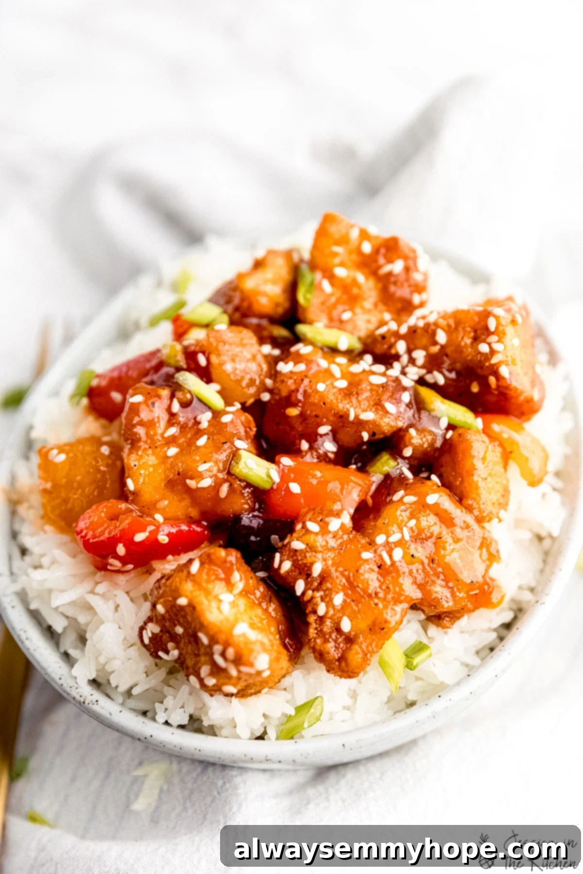 Crispy Vegan Sweet and Sour Tofu 7 A beautifully plated bowl of sweet and sour tofu on white rice, with a fork on a napkin, ready to be enjoyed.