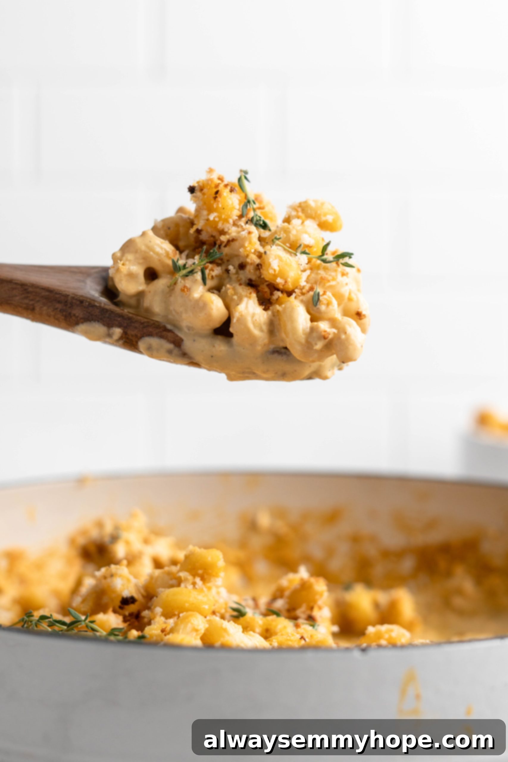 A spoonful of creamy baked vegan mac and cheese being lifted from a skillet, showcasing its perfect texture and rich sauce.