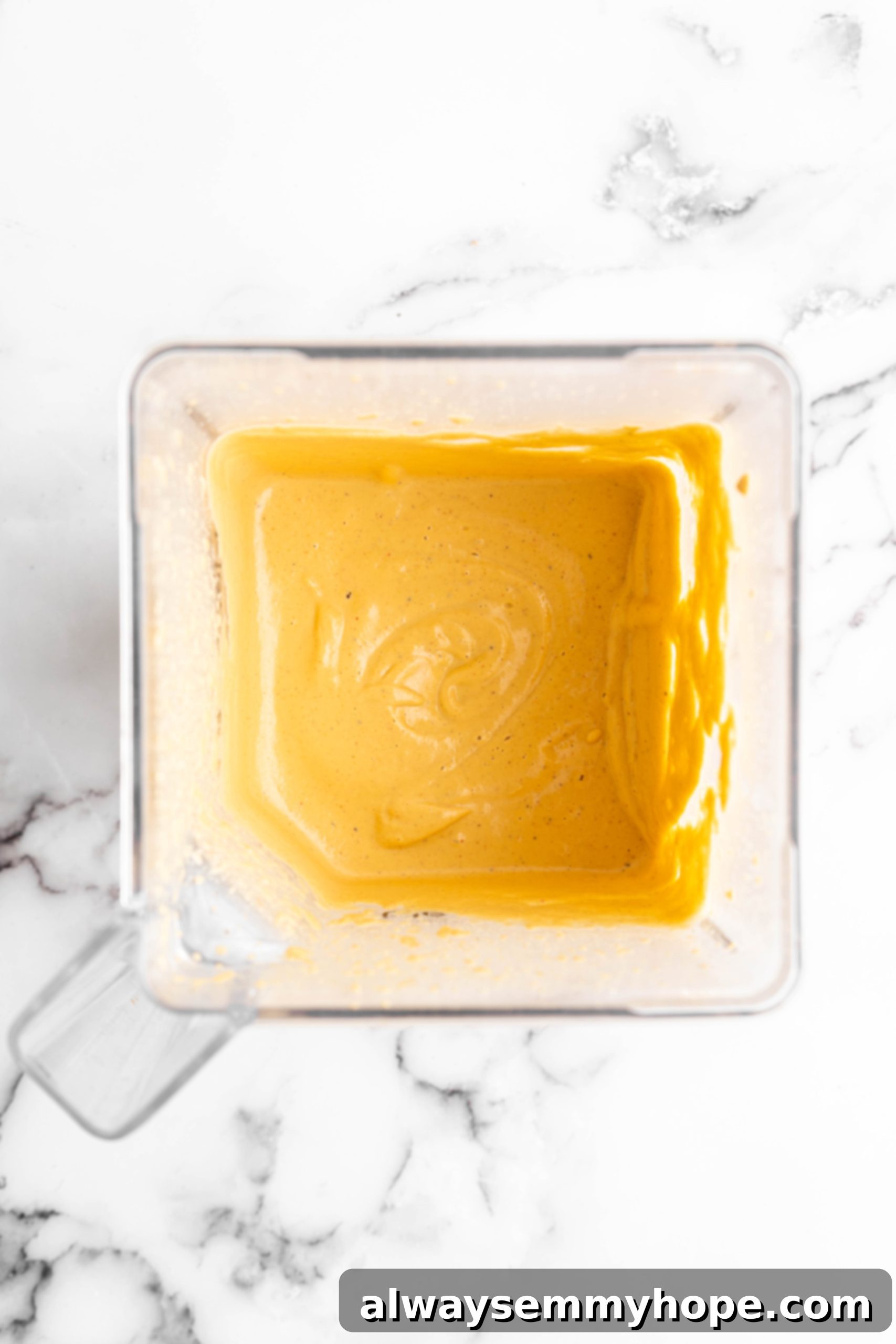 Overhead view of all vegan cheese sauce ingredients in a high-speed blender, ready to be processed into a smooth, creamy sauce.