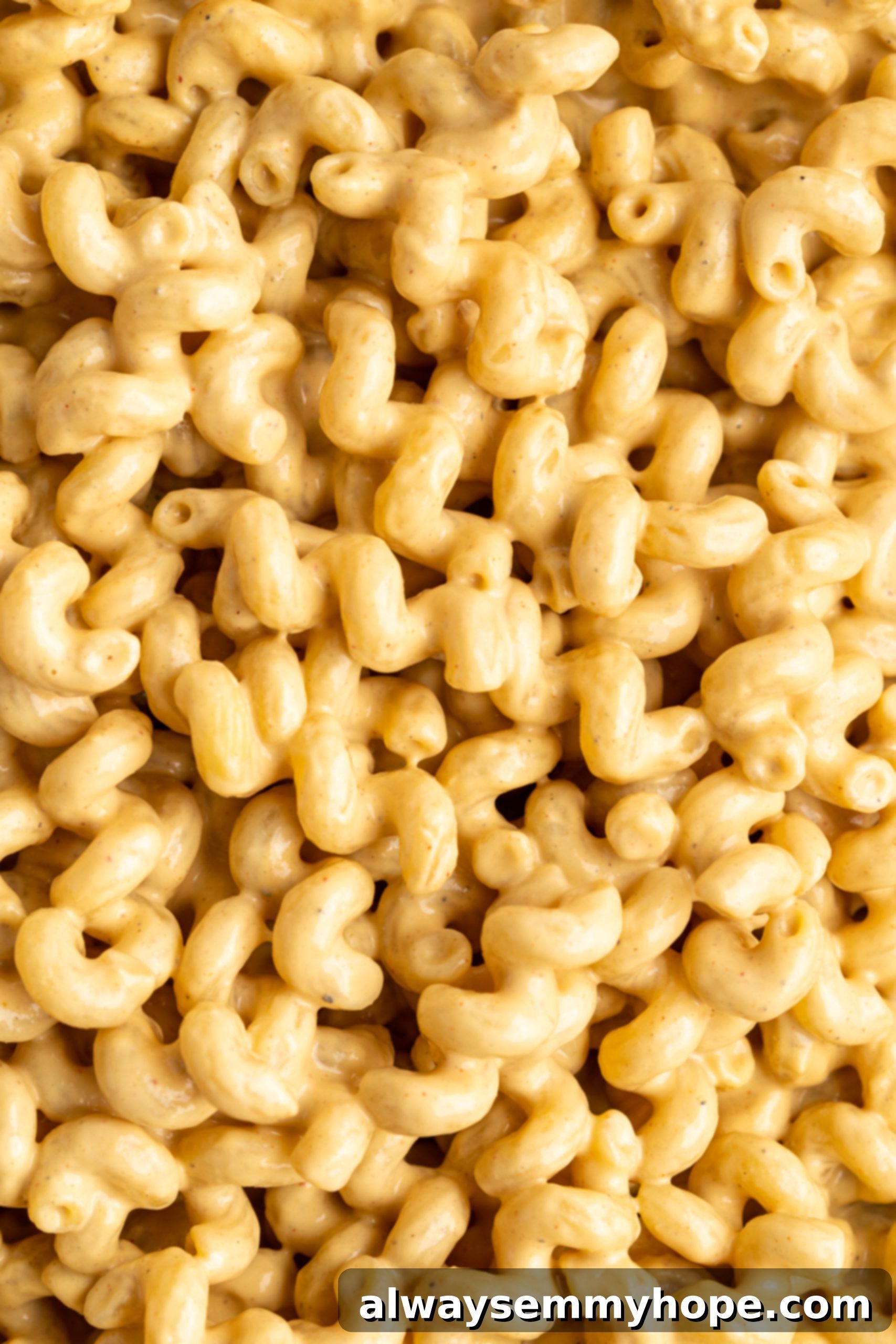 Close-up shot of vegan mac and cheese in a pan, highlighting the creamy texture and even coating of the pasta, showing it's perfectly mixed before baking.