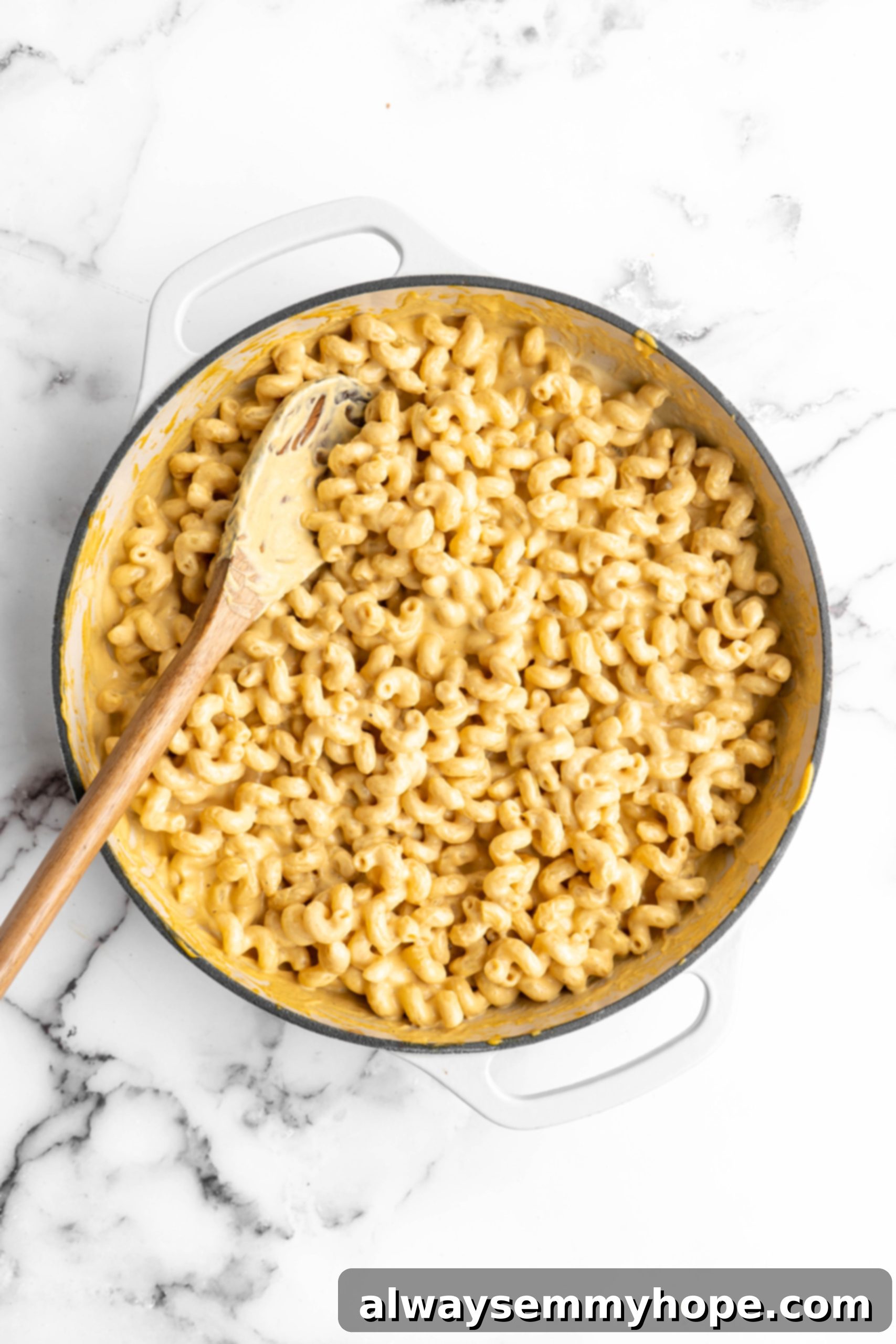 Vegan mac and cheese in a baking dish, perfectly mixed and ready for the breadcrumb topping, with a wooden spoon resting inside.