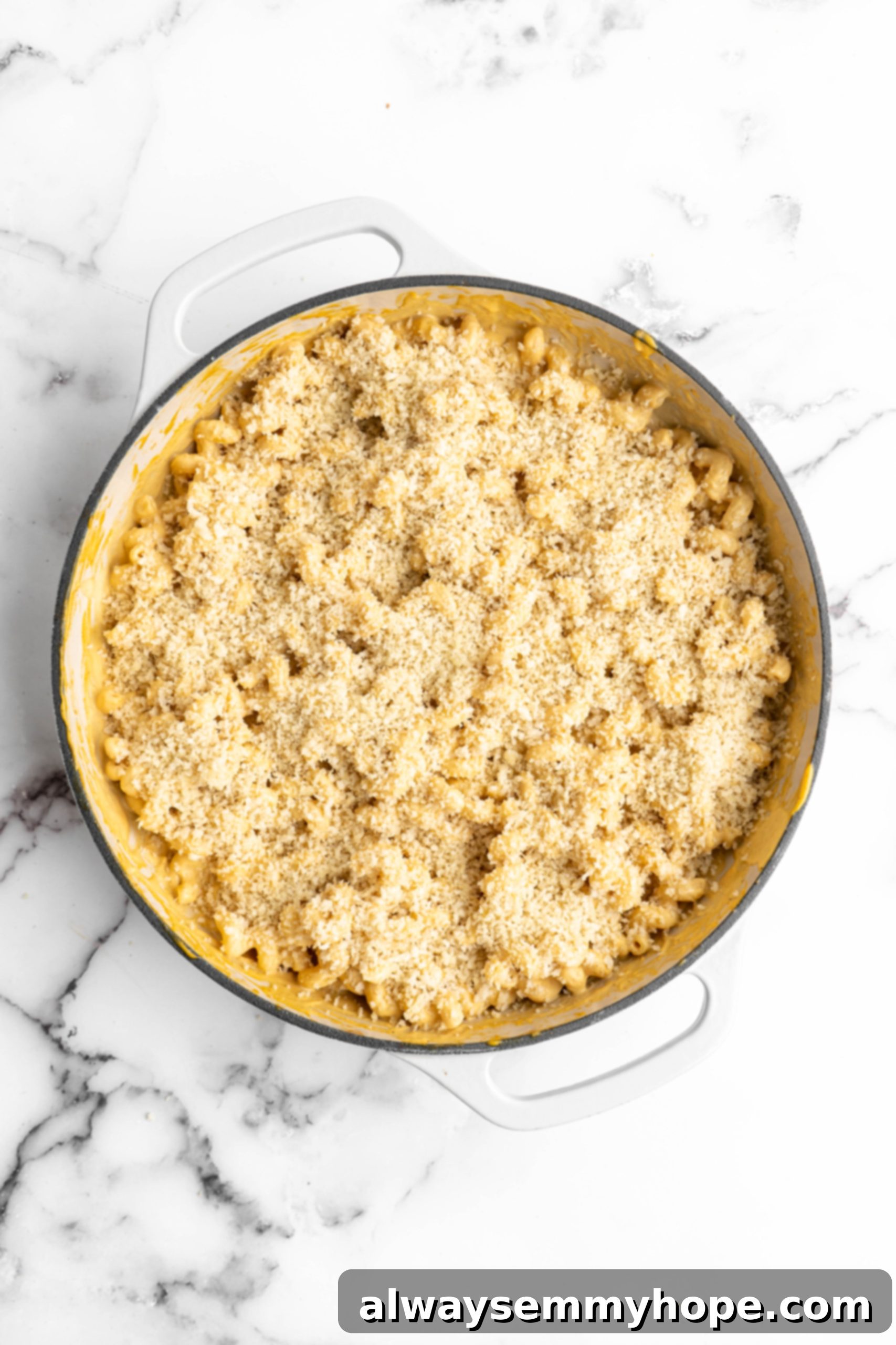 Unbaked vegan mac and cheese in a pan, topped with a generous layer of seasoned breadcrumbs and optional vegan shredded cheese, ready to be baked to golden perfection.