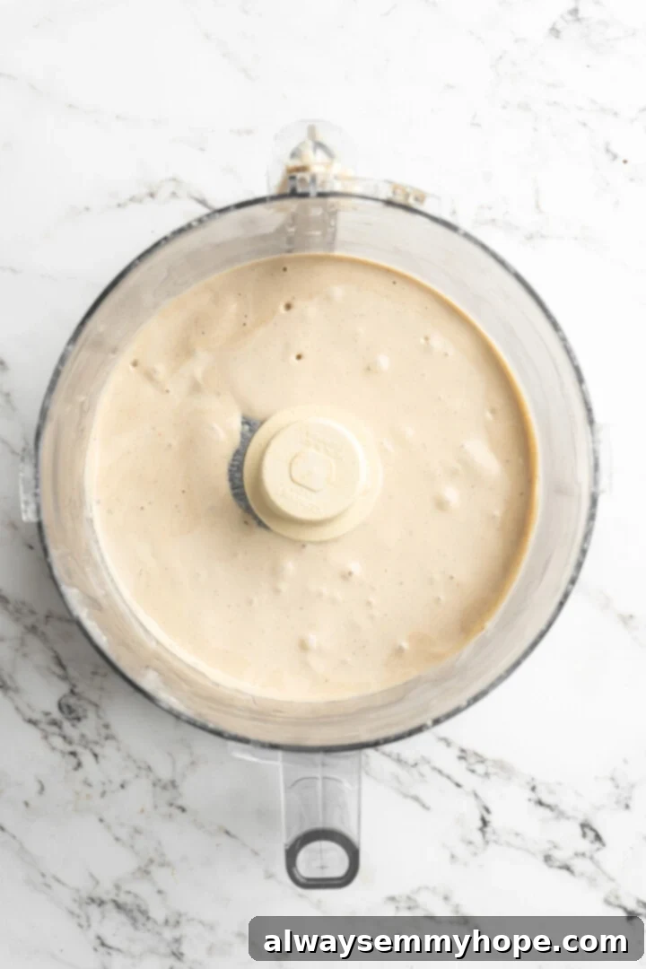 Silky smooth cashew cream, the heart of your vegan spinach artichoke dip. A smooth, off-white cashew cream mixture filling the bowl of a food processor after blending, forming the rich base for the dip.