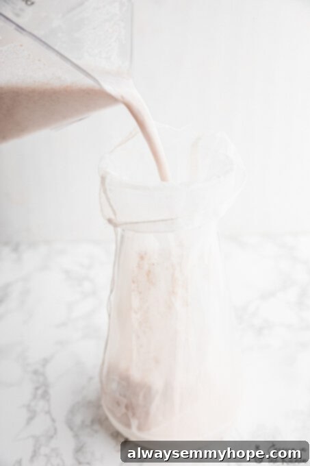 Pouring freshly blended almond milk into a nut milk bag over a large bowl for straining