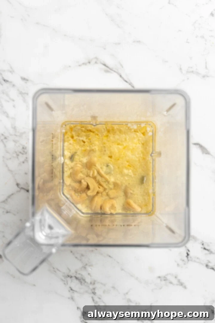 Close-up of soaked cashews and other liquid ingredients in a high-speed blender jar, ready to be blended into vegan butter.