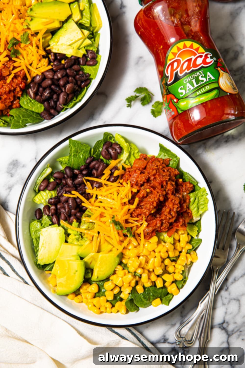 Taco salad in bowls with a jar of salsa and fresh ingredients