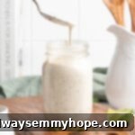 A spoon artfully drizzles creamy, homemade vegan ranch dressing into a clear glass jar, showcasing its smooth texture and rich appearance.