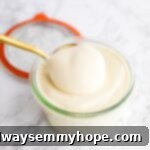 A spoon gracefully scoops thick, creamy homemade vegan mayo from a glass jar, demonstrating its perfect consistency.