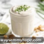 A glass jar filled with luscious vegan sour cream, beautifully garnished with fresh green chives on top.