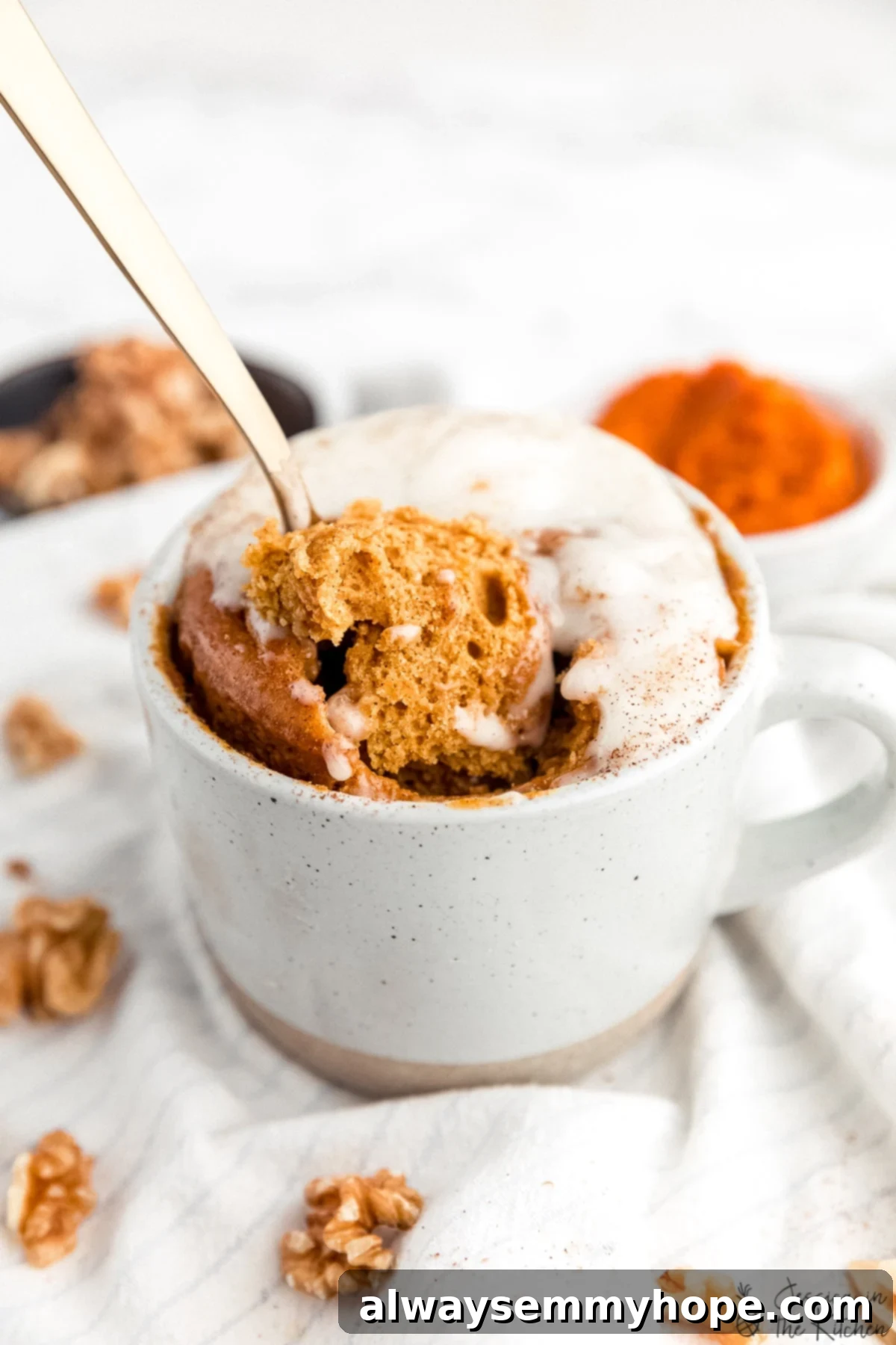 Gold spoon being pushed into and scooping out a piece of pumpkin cake out of a mug, showcasing its moist texture.
