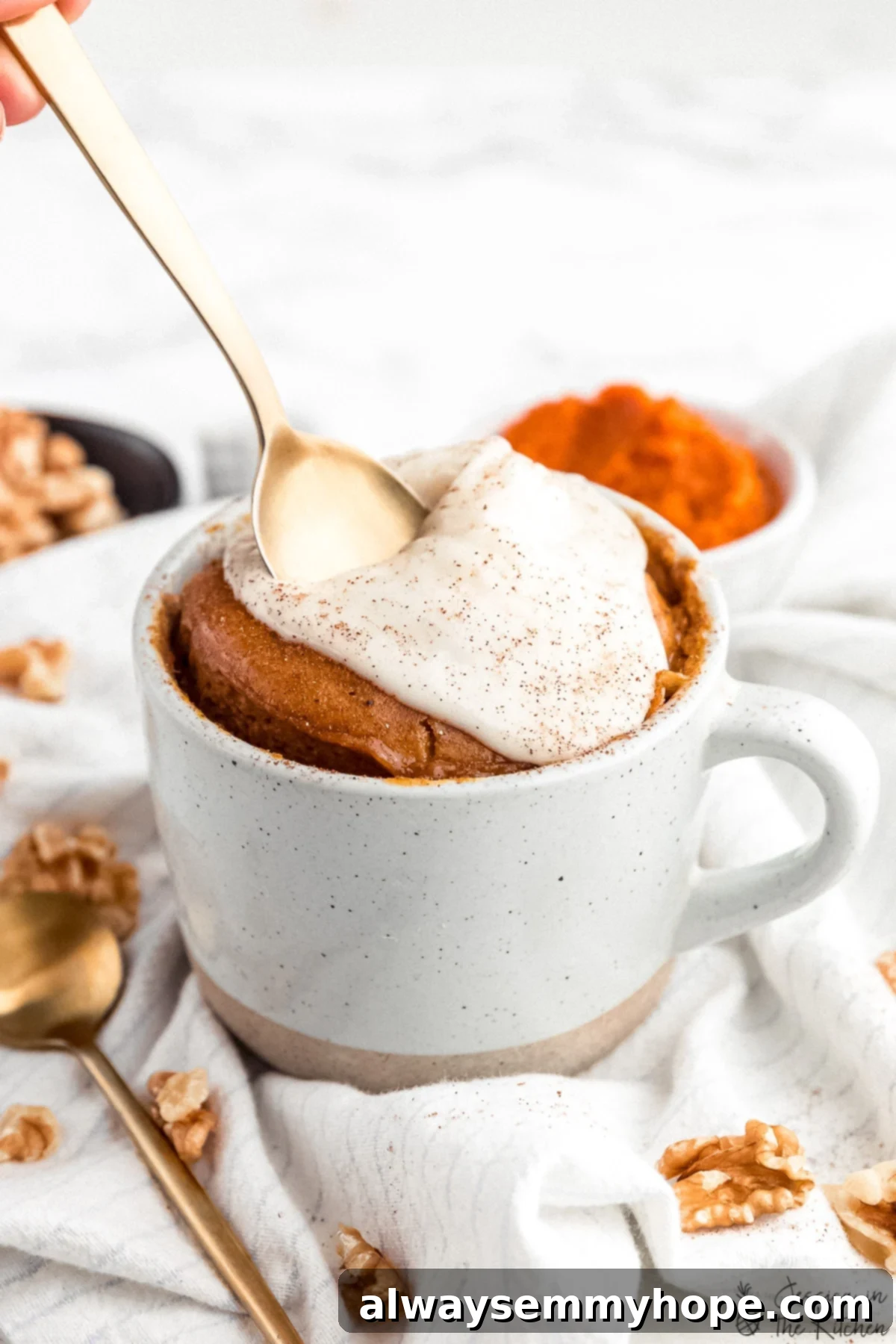 Gold spoon being pushed into a pumpkin mug cake with a generous layer of vegan cream cheese frosting.