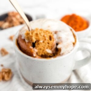 Gold spoon being pushed into and scooping out a piece of pumpkin cake out of a mug, topped with frosting.