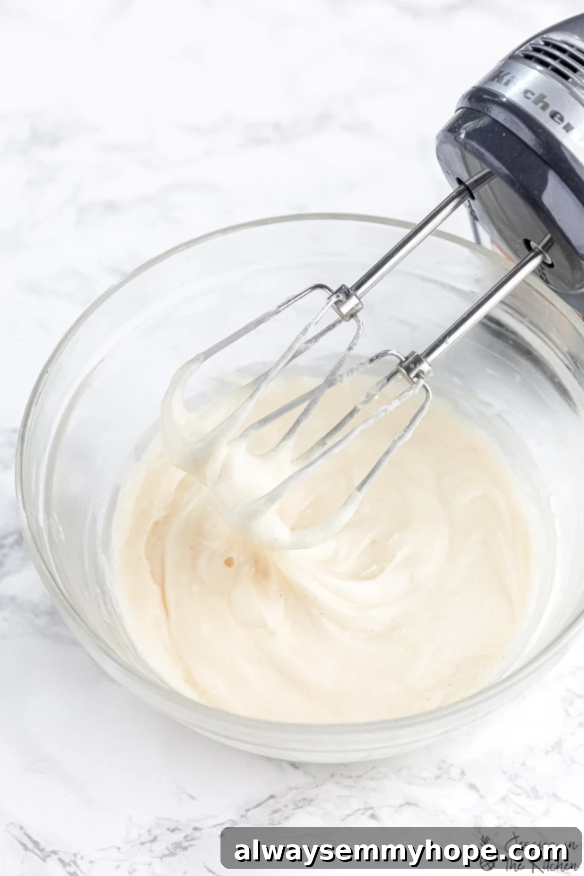 Frosting in a glass bowl with hand mixer scooping some out.