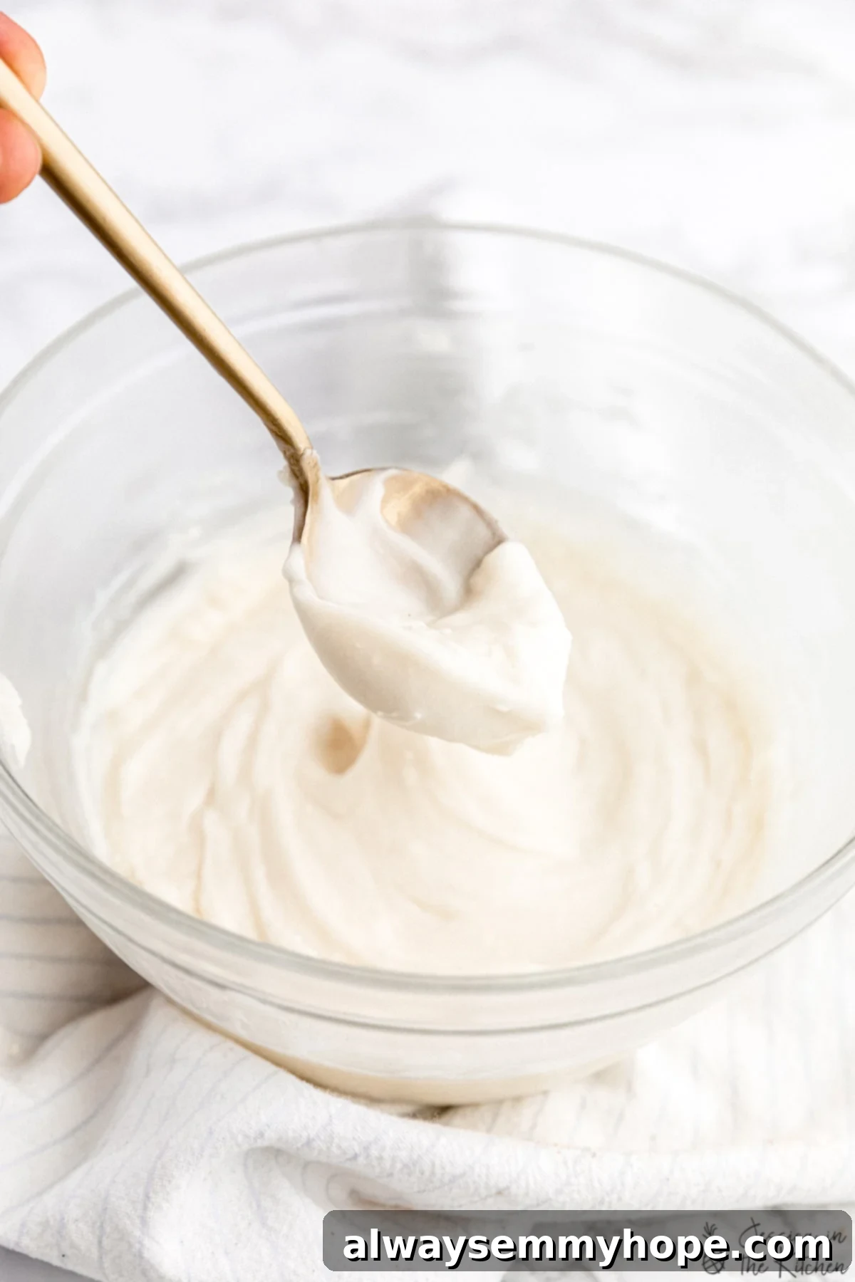 Frosting being spooned out of a glass bowl with a gold spoon.