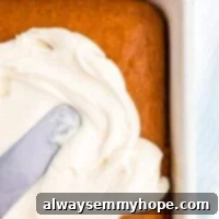 Velvety Vegan Cream Cheese Frosting 5 Cream cheese frosting spread across an orange pumpkin cake with a silver offset spatula.