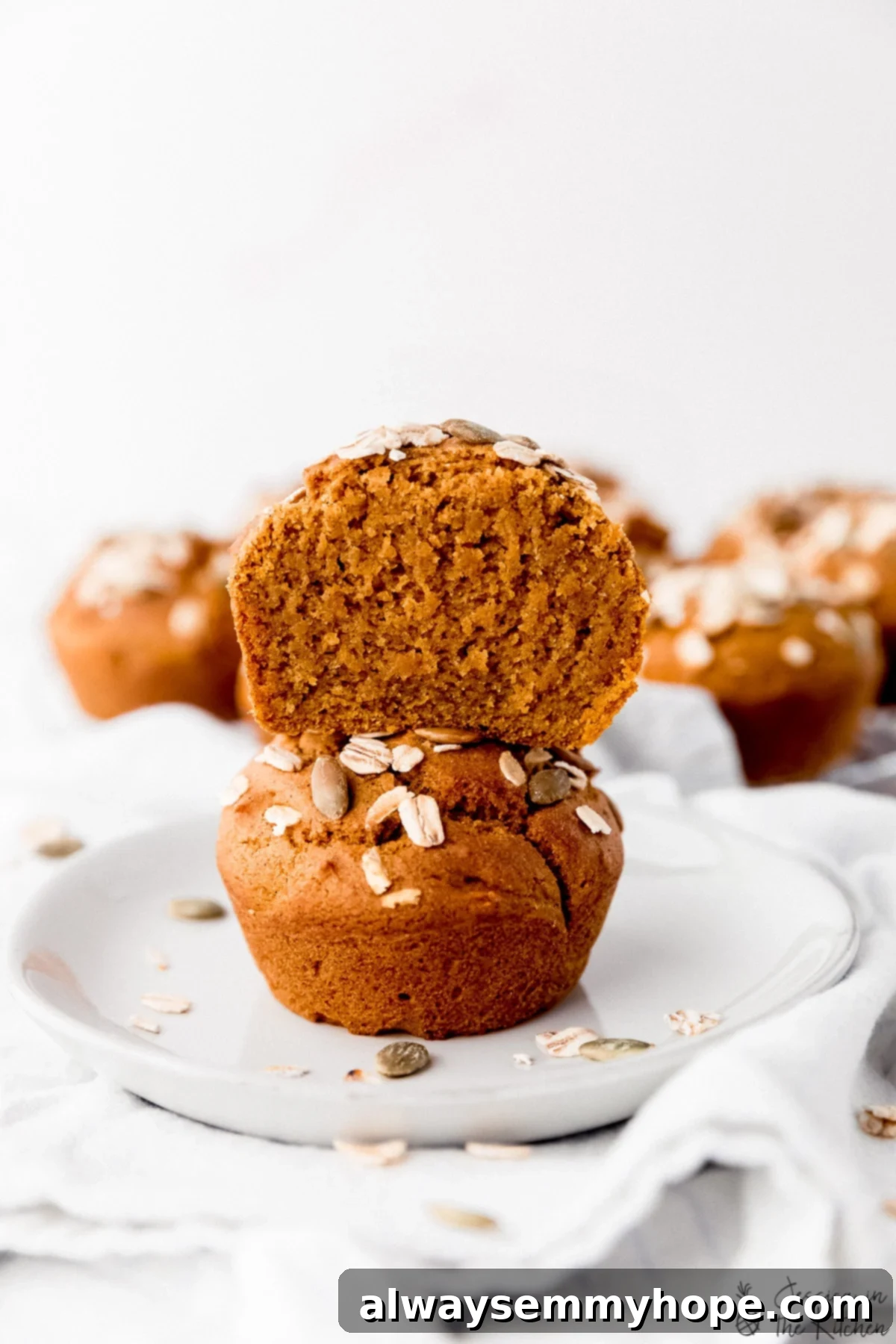 Two vegan pumpkin muffins on a plate one is cut in half and stacked on top of the other, showcasing the moist interior.