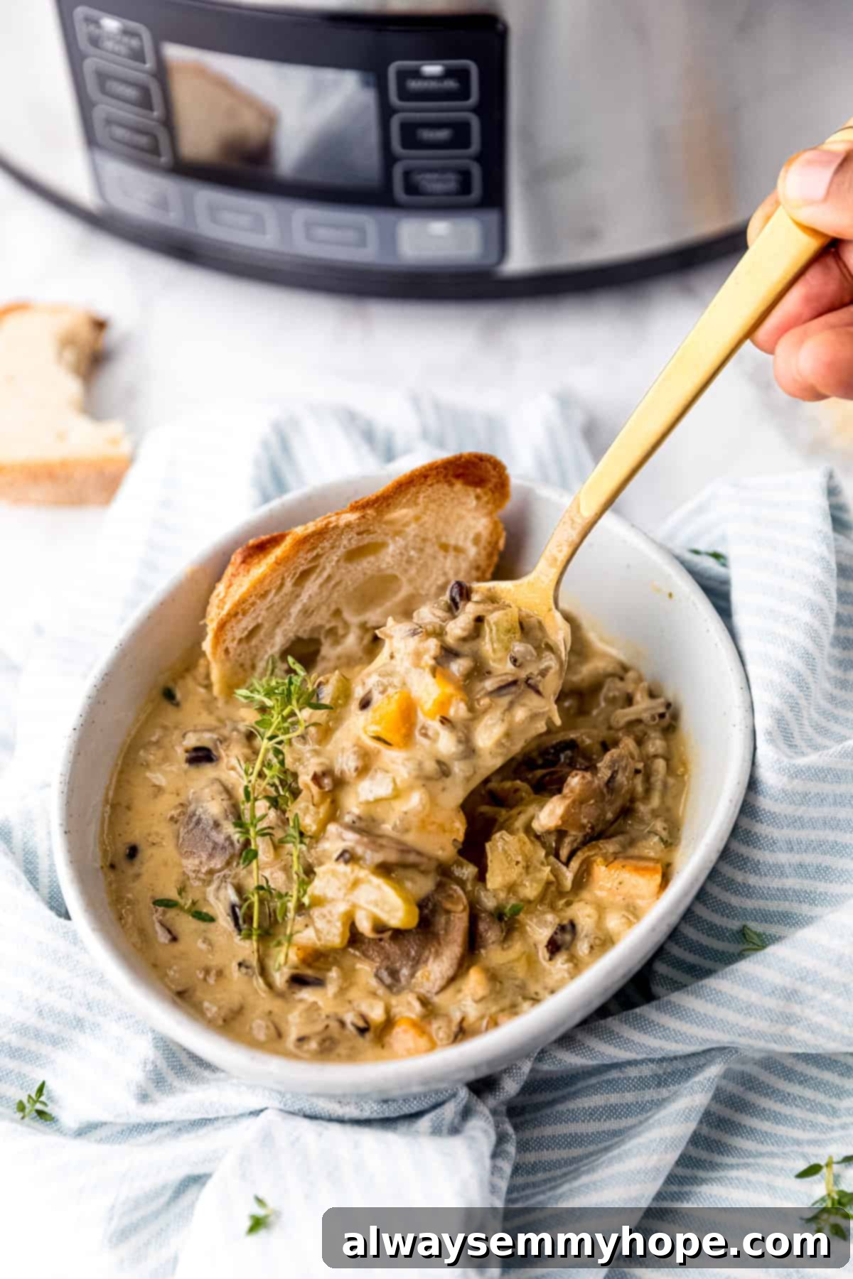 A bowl of creamy mushroom wild rice soup with a spoon scooping a portion, the slow cooker visible in the background.