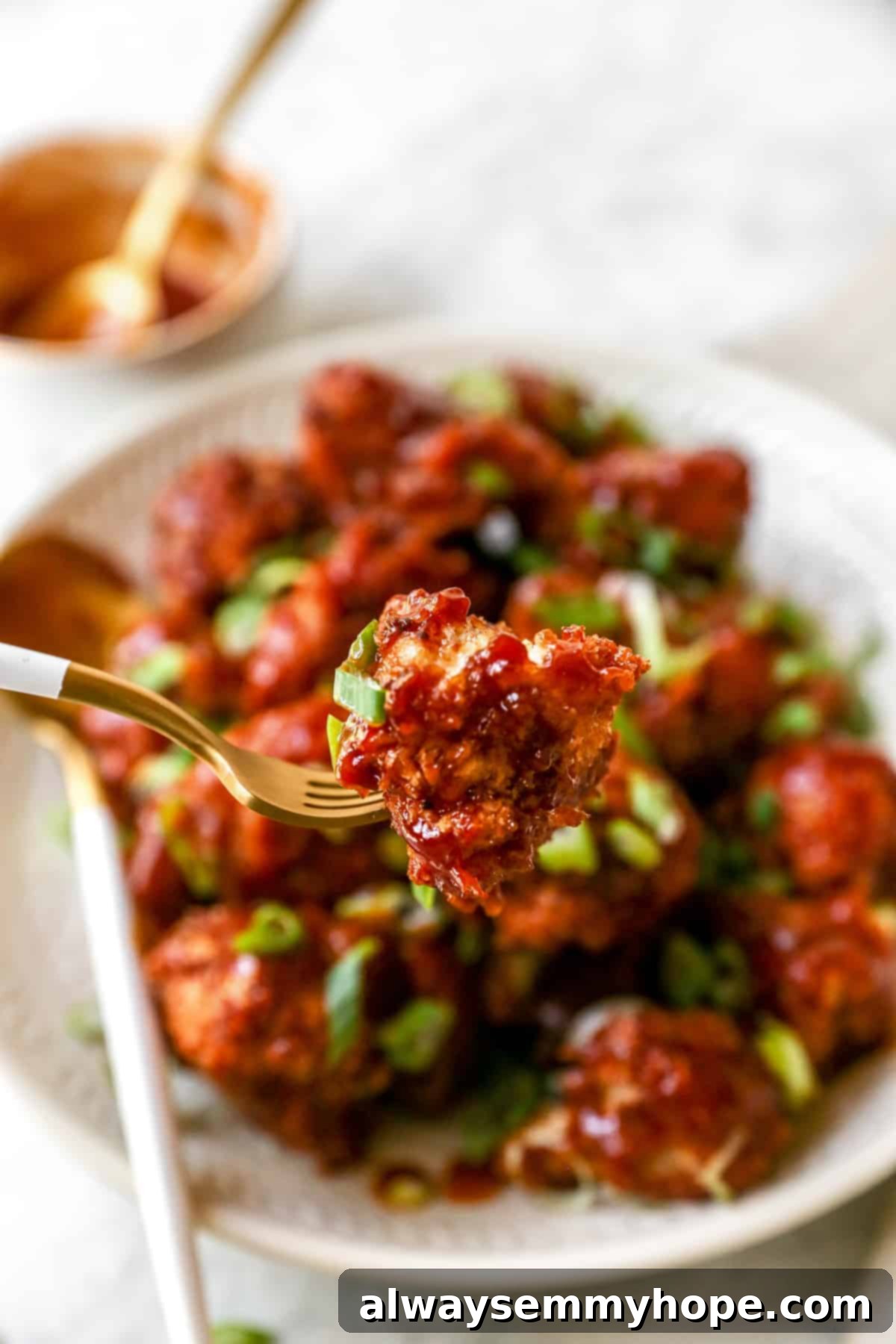 BBQ cauliflower wings are perfect for game day appetizers or make them your main dish on a weeknight. So easy and delicious! Close up of a bbq cauliflower wing on a fork with a plate of cauliflower wings in the background.