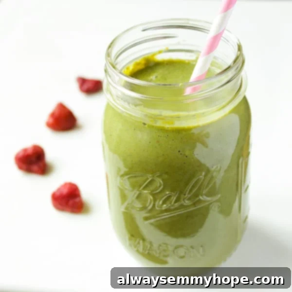 Strawberry kale smoothie in mason jar with pink and white striped straw, garnished with fresh strawberries and kale leaves