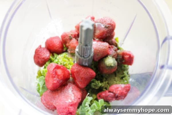 Overhead view of fresh kale and frozen strawberries neatly placed in a blender, ready to be mixed into a smoothie