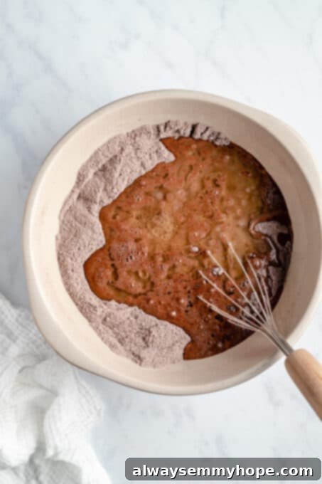 Liquid oil being poured into the dry ingredients for vegan chocolate cake, illustrating the start of combining wet and dry.