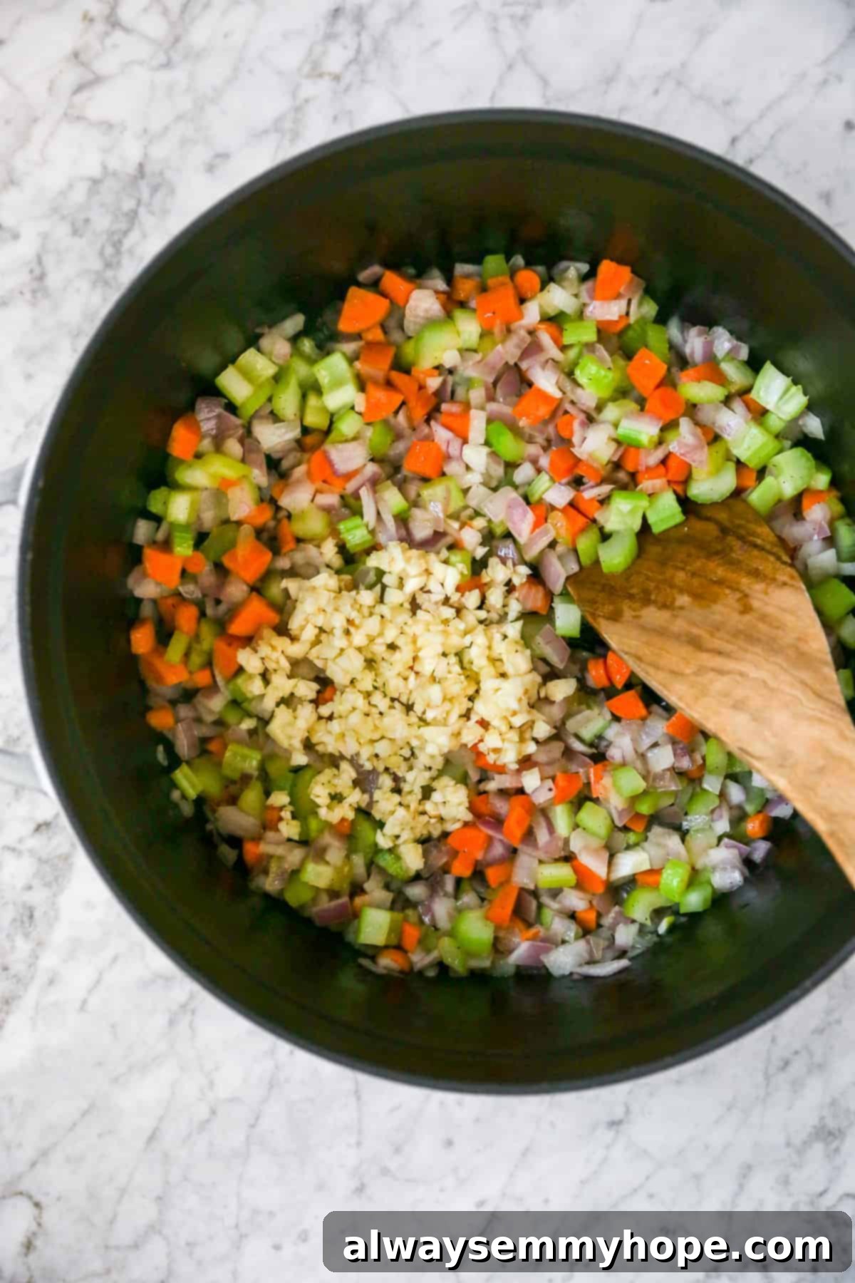 Adding minced garlic to the sautéed mirepoix in the pot, stirring to combine and cook until fragrant for the white bean soup base.