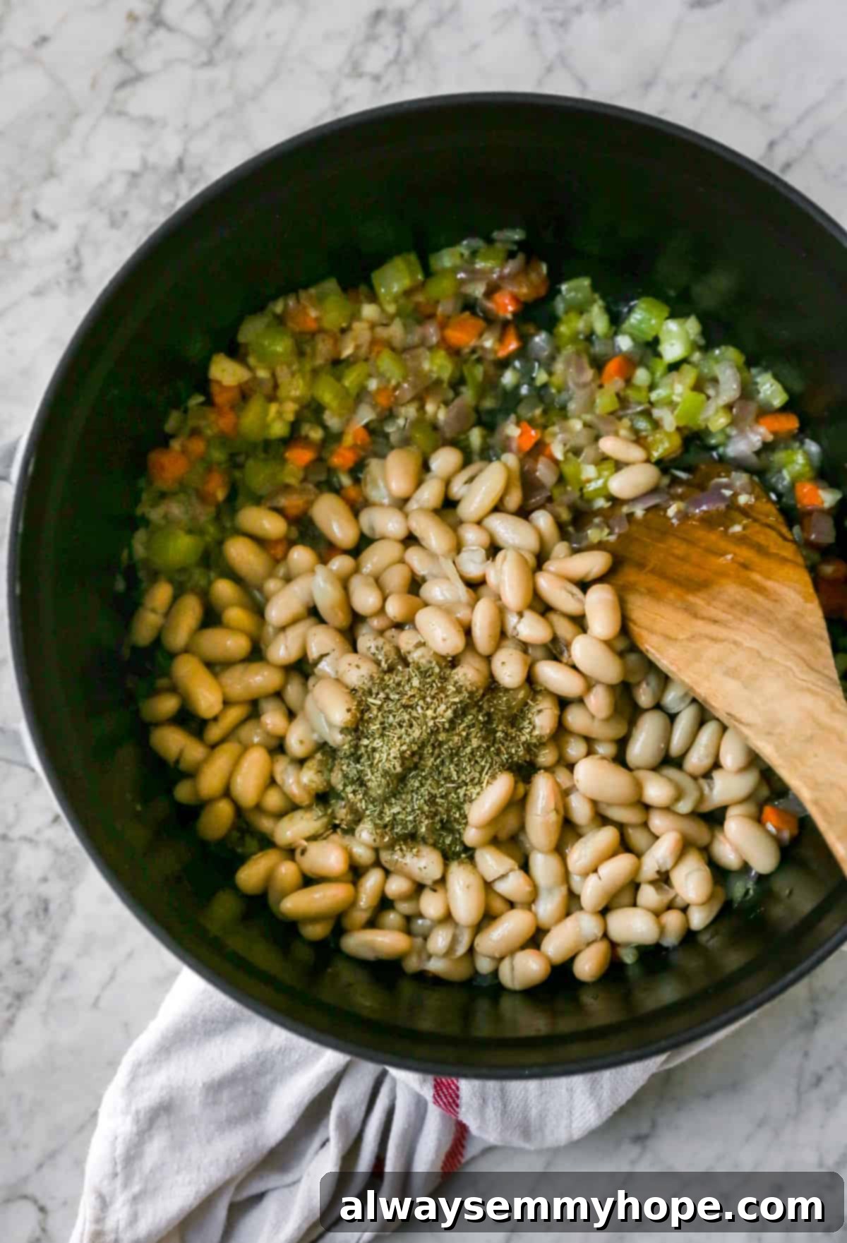 Adding Italian seasoning and white kidney beans to the sautéed vegetables, stirring them together to infuse flavors for the soup.