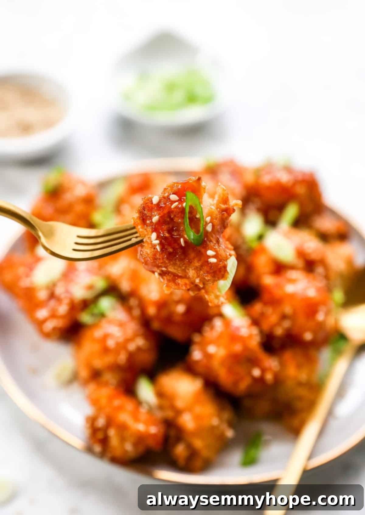 Crispy Sweet and Sour Cauliflower Wings 11 A golden fork lifts a perfectly coated sweet and sour cauliflower wing above a plate brimming with more delicious wings.