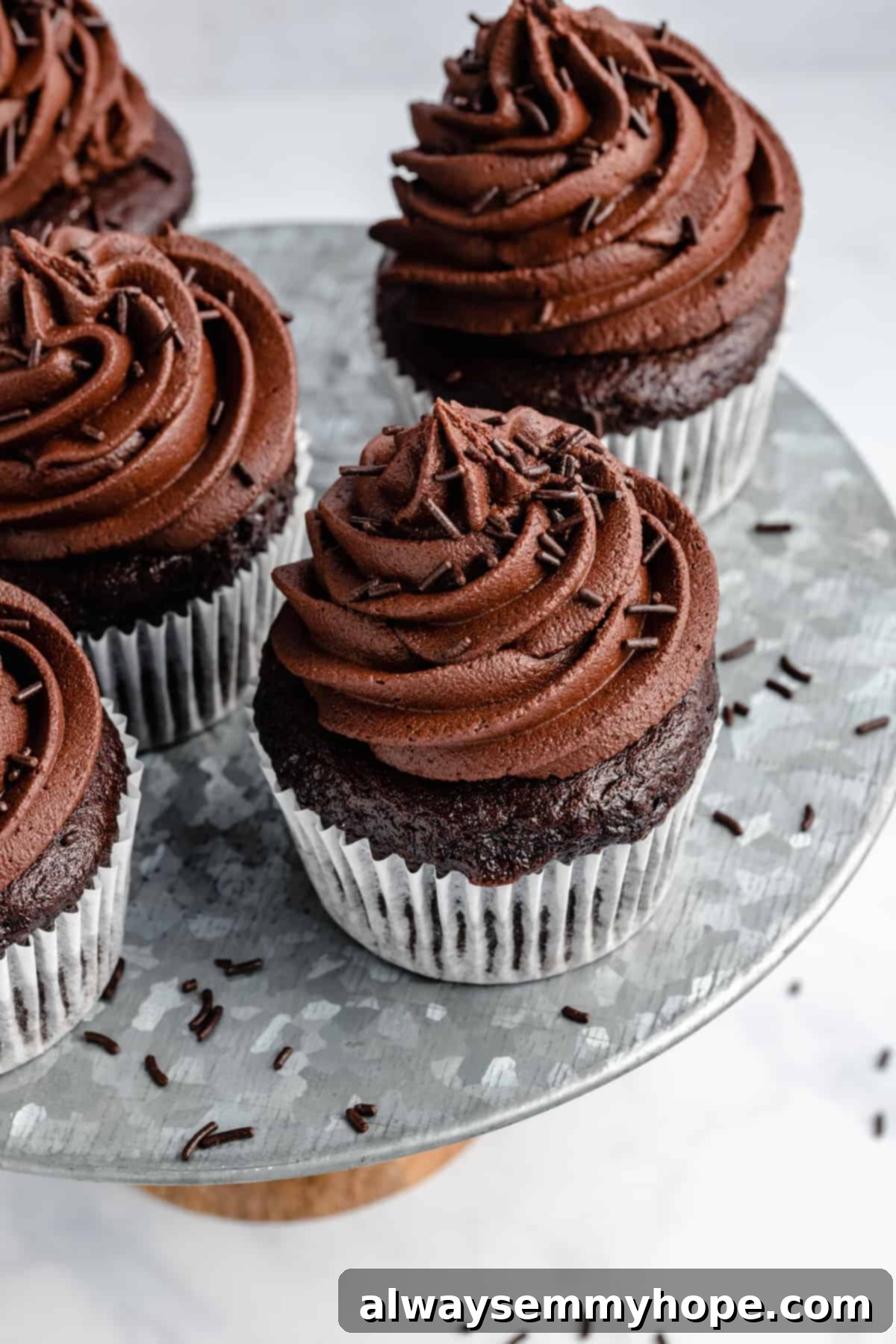 Decadent Dairy-Free Chocolate Cupcakes 10 five chocolate cupcakes with frosting and sprinkles on a tiered metal cake stand