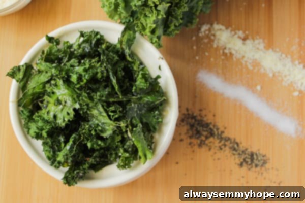 A bowl of homemade kale chips, perfectly seasoned and ready to eat. Crispy seasoned green kale chips in a bowl, with a small dish of seasoning on the side.