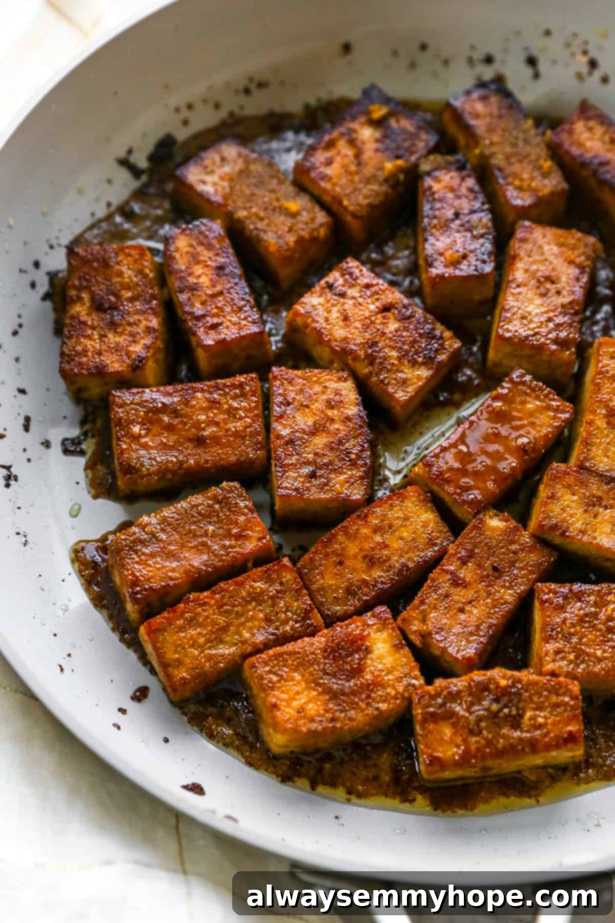 Cooked and browned marinated tofu pieces in a pan, coated with the thickened sauce.