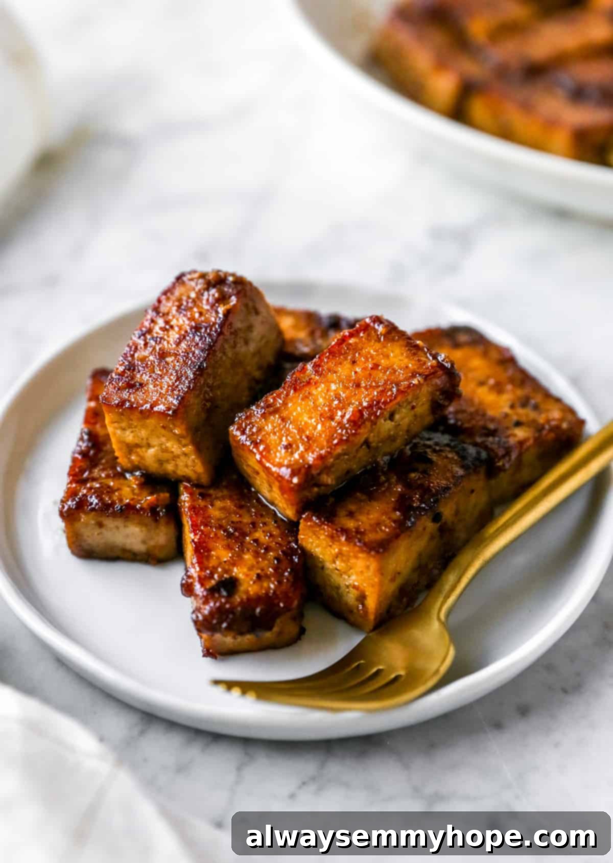 A close-up shot of marinated and cooked tofu on a plate, with a gold fork piercing a piece, emphasizing its texture.