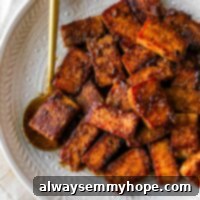 Crispy, golden-brown marinated tofu pieces on a plate, ready to serve, with a gold spoon holding some tofu.