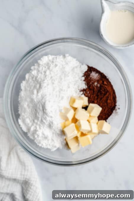 Powdered sugar, butter, and cocoa powder in a glass mixing bowl, ready to be mixed