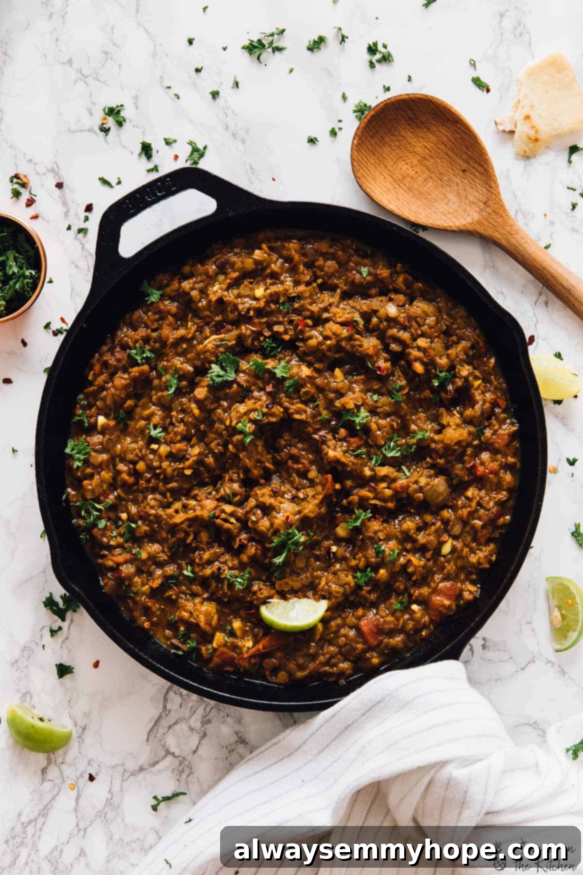 A large cast iron skillet filled with perfectly cooked brown lentils, garnished with fresh parsley, next to a wooden spoon.