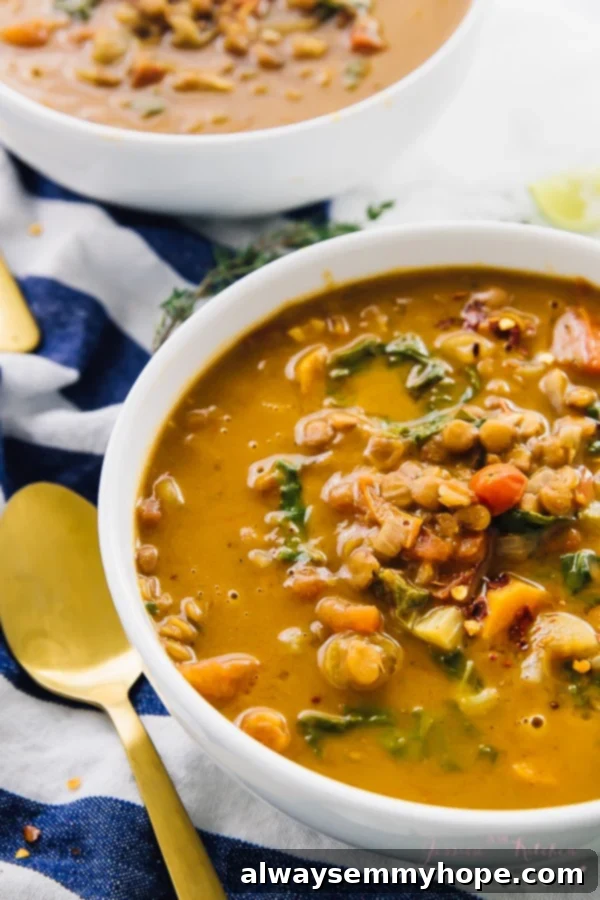 A beautiful broth-based vegetable soup, generously packed with vibrant kale, tender carrots, and wholesome lentils, served in a pristine white bowl.