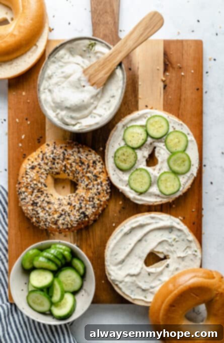Two bagel halves topped with homemade vegan cream cheese and fresh cucumber slices, arranged on a rustic cutting board.