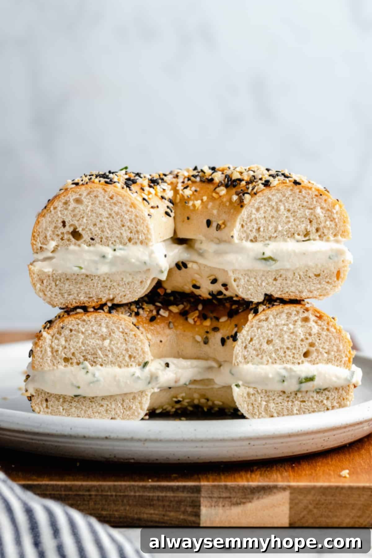 A toasted bagel generously spread with homemade vegan cream cheese and cut in half, displayed on a wooden surface.