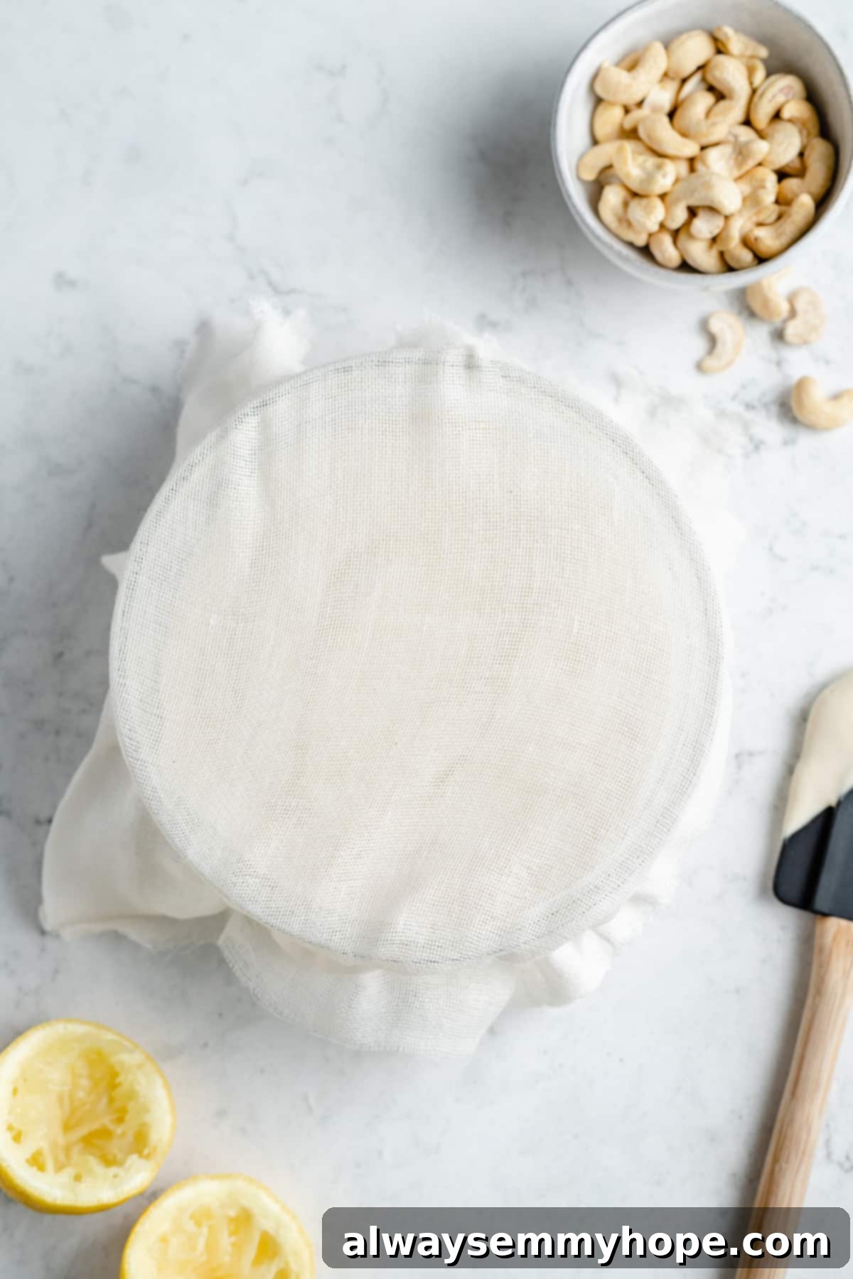 A glass bowl of vegan cream cheese covered with cheesecloth and secured with a rubber band, fermenting in a warm place.